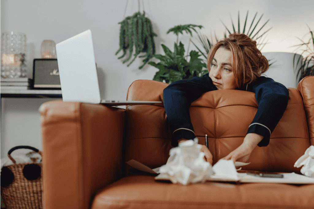 Woman feeling overwhelmed and mentally exhausted while sitting on couch with laptop, representing productivity pressure and anxiety