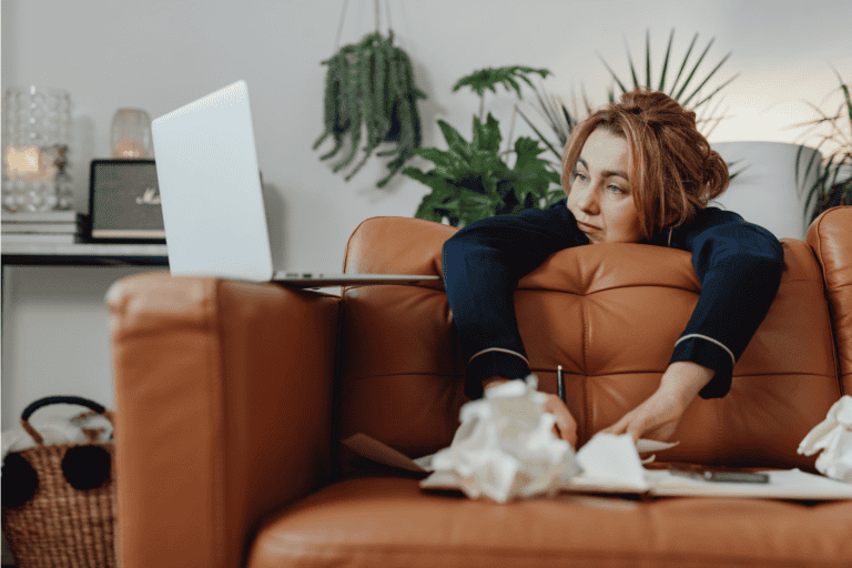 Woman feeling overwhelmed and mentally exhausted while sitting on couch with laptop, representing productivity pressure and anxiety