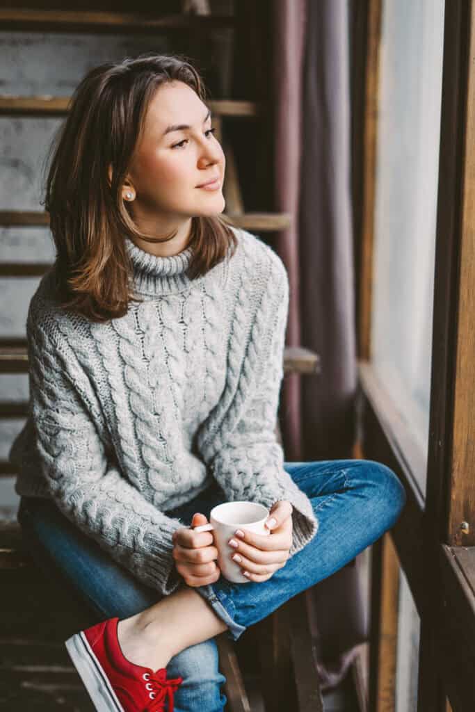 Woman holding a mug and looking thoughtfully out a window, illustrating a section about anxiety, overthinking, and self-doubt.